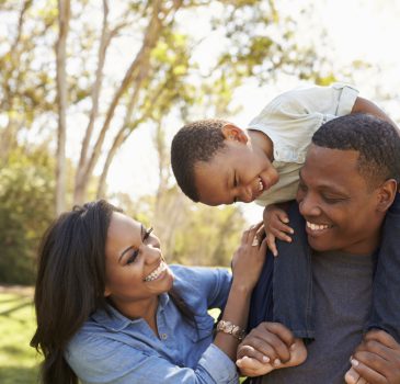 Parents Carrying Son On Shoulders As They Walk In Park