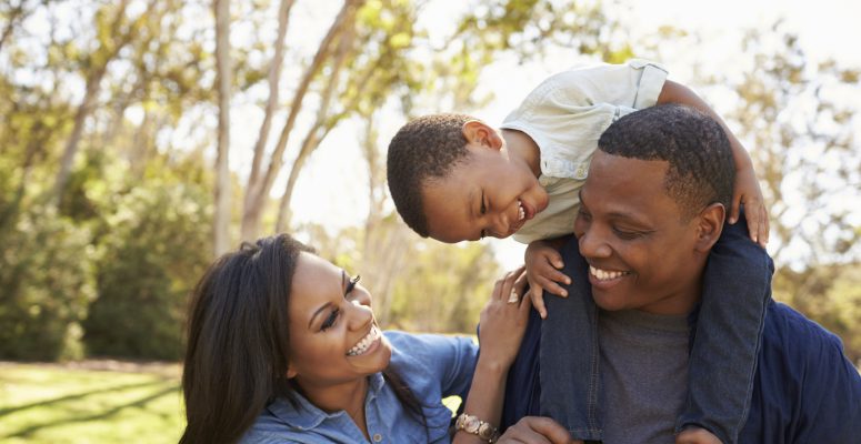 Parents Carrying Son On Shoulders As They Walk In Park