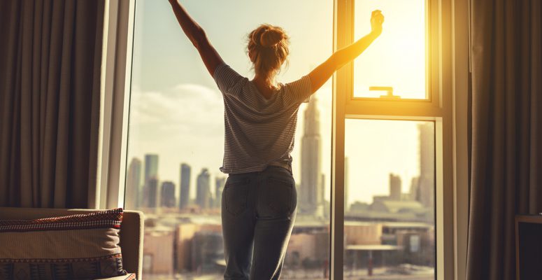 happy woman stretches and  opens curtains at window in morning